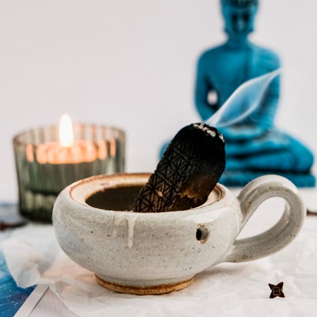 Calming scene with a burning palo santo in a ceramic pot alongside a candle and Buddha figurine.