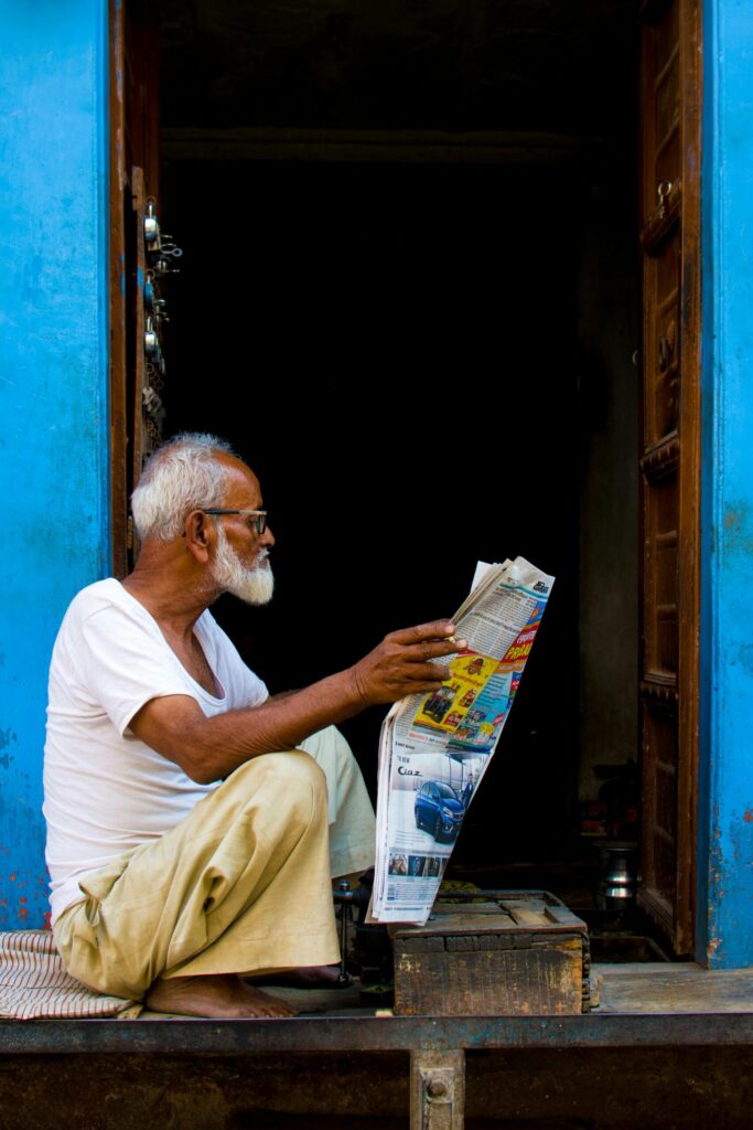 Senior man in white shirt reading a newspaper in a vibrant blue doorway in Bikaner, India.